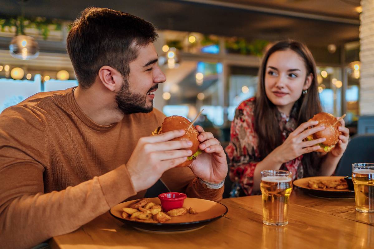 national burger day - a couple holding burger in their hands while sitting in a restaurant